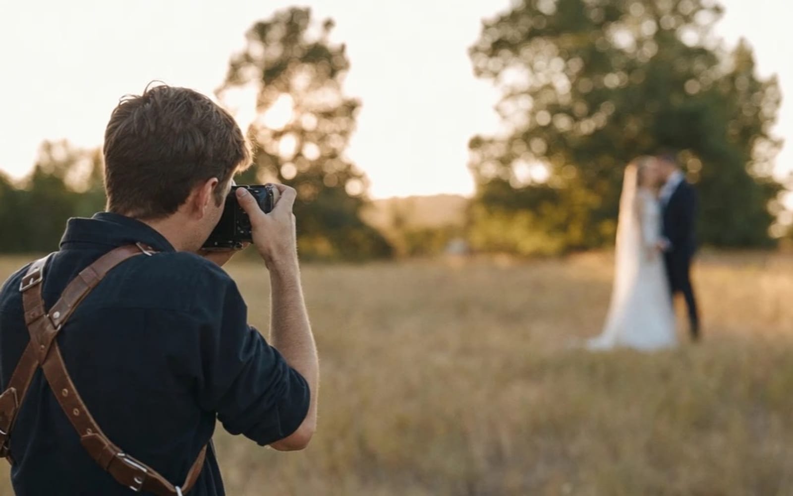 A wedding photographer photographing a couple in a meadow at golden hour